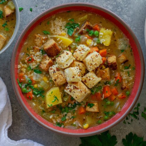Bowl of creamy vegan chicken pot pie soup topped with crispy tofu, peas, and golden puff pastry croutons, garnished with parsley and parmesan