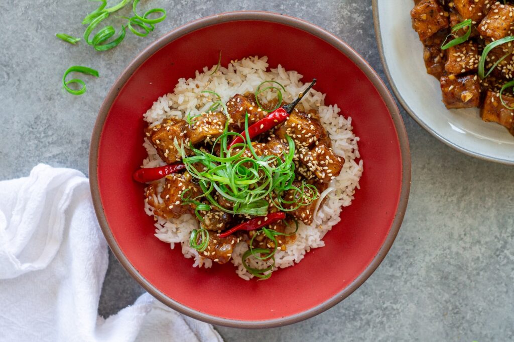 Vegan honey garlic tofu served over white rice with sesame seeds and green onion garnish